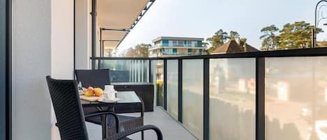 Ein Balkon mit Tisch und Stühlen, einer Glasbrüstung und Blick auf Gebäude und Bäume.