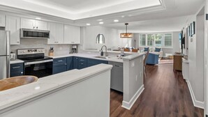 Une cuisine moderne avec des meubles blancs, un îlot central et un coin repas doté de chaises bleues.
