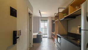 A narrow hotel corridor with a kitchenette on the right, a bed with a view to the outside, and a door on the left. - Modern Retreat Near Allianz Parque Sp-p1604a (São Paulo)