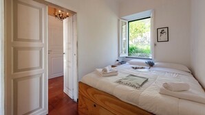 A bedroom with a wooden bed, white bedding, a window with a view of greenery, and a chandelier.