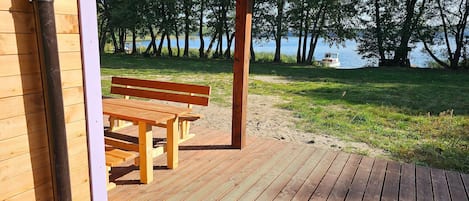A wooden deck with a bench, a covered area, and a view of a lake with trees.