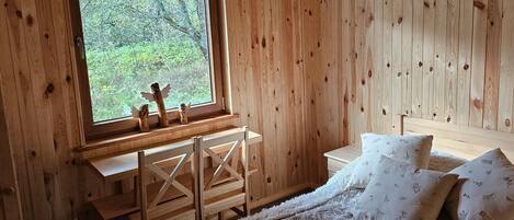 Un dormitorio de cabaña de madera con un ventanal grande, muebles de madera y una cama acogedora.