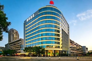 A multi-story hotel with a curved facade, large windows, and a red logo on top.