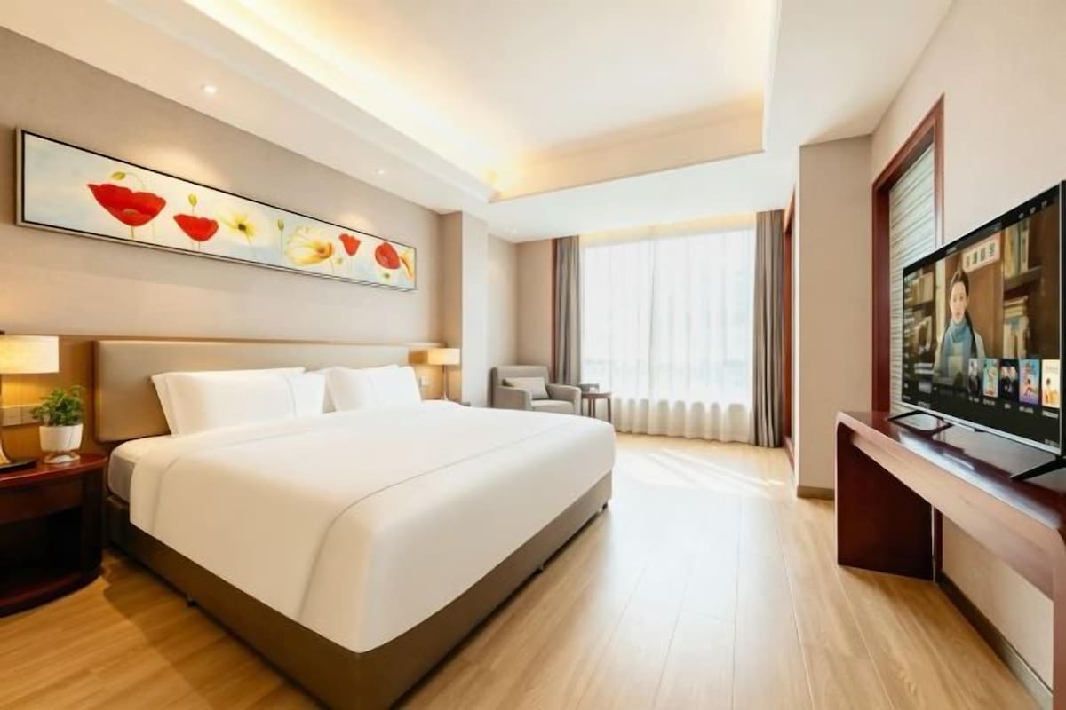 A hotel room with a large bed, a television, a desk, and a painting on the wall.