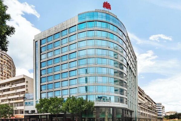 A modern hotel with a curved facade, multiple floors, and a prominent red logo on the top.