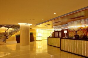 A hotel lobby with a reception desk, a staircase, and a large pillar.