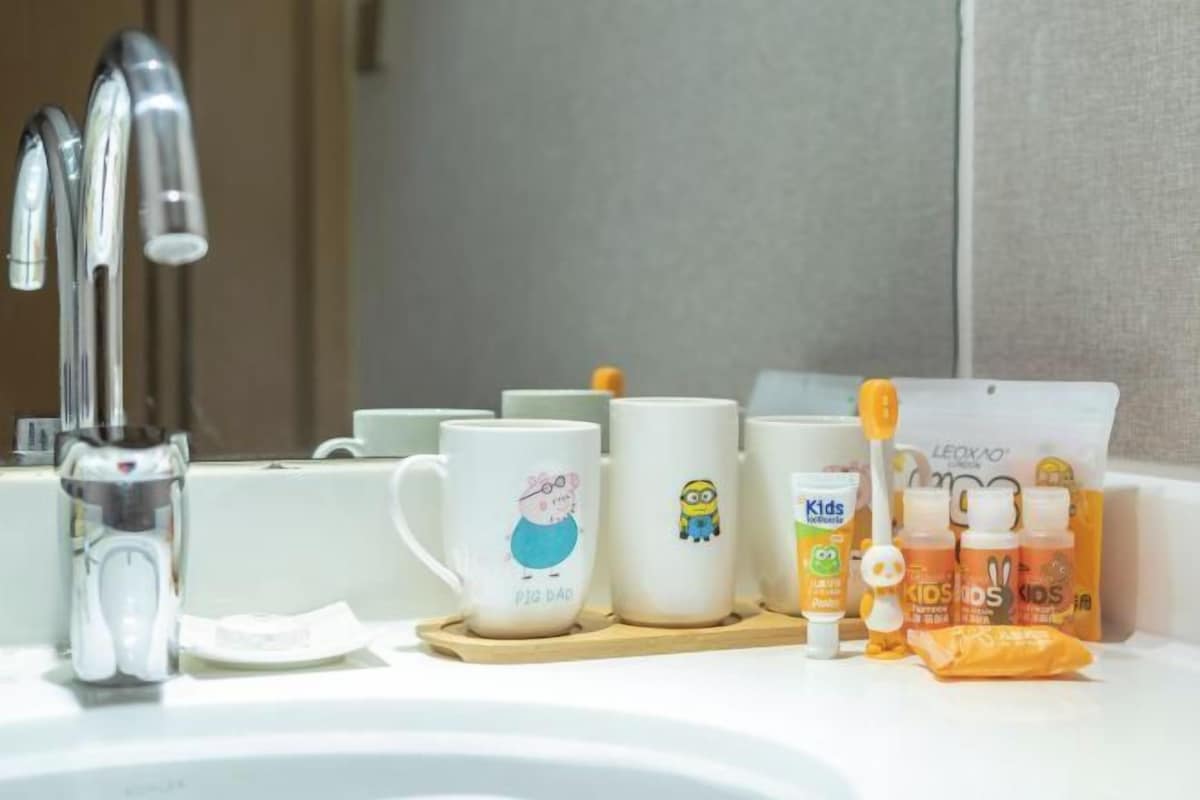 A bathroom sink with a faucet, three mugs with cartoon characters, and children's toothpaste.