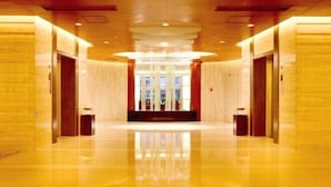 A spacious, well-lit hallway with polished floors and wooden paneling, leading to a reception area with a chandelier. - Hotel Brilliant（Quanzhou South Station Store） (Shishi)