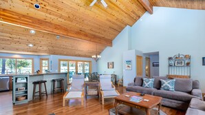 A spacious living area with wooden flooring, a grey sofa, a wooden coffee table, and a kitchen area with a bar stool and a sink. - OREG36-Family and Dog Friendly Retreat w. AC (Sunriver)