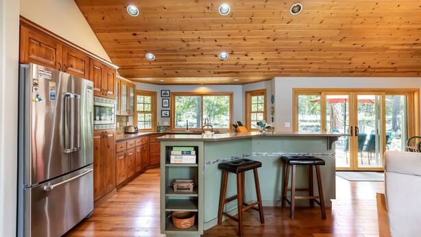 A spacious kitchen with wooden cabinets, a stainless steel refrigerator, and a large island with stools. - OREG36-Family and Dog Friendly Retreat w. AC (Sunriver)