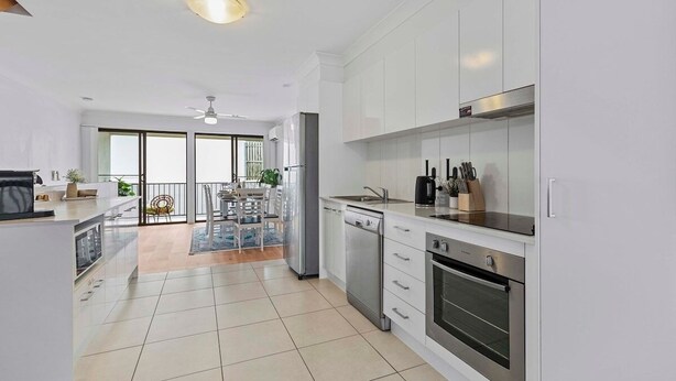 A modern kitchen with white cabinets, stainless steel appliances, and a large window. - Central Redcliffe Coastal Home Walk to Beach (Redcliffe)