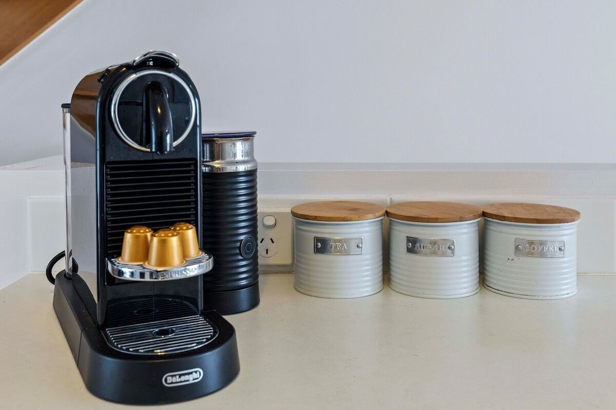 A Delonghi espresso machine with three cups, two metal containers, and three metal containers with lids.