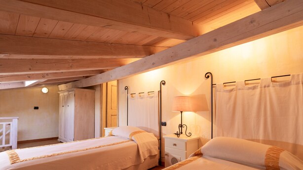 A room with two beds, wooden beams on the ceiling, a bedside table with a lamp, and a wardrobe. - Casa Onda Marina by Wonderful Italy (Olbia)