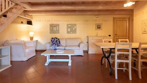 A spacious living area with a wooden staircase, a sofa, a coffee table, and a dining table with chairs. - Casa Onda Marina by Wonderful Italy (Olbia)