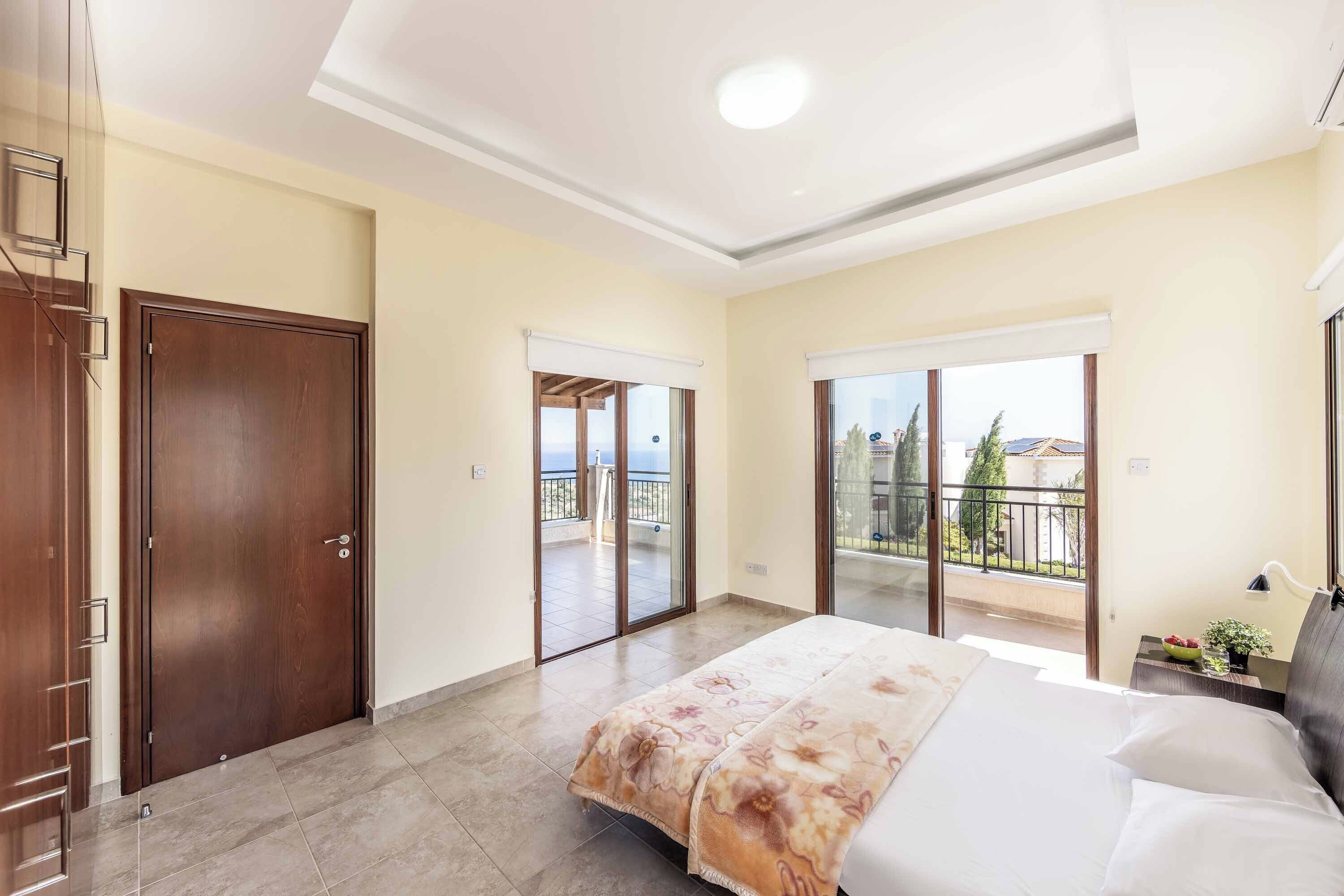 Quarto com cama, mesa de cabeceira, janela e porta para varanda.