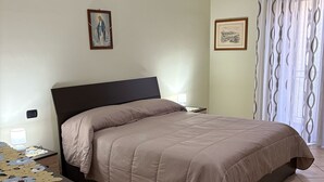 Un dormitorio con cama, mesita de noche, lámpara y ventana con cortinas.