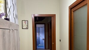 Un pasillo con una puerta de madera a la derecha, un cuadro en la pared y una lámpara arriba.