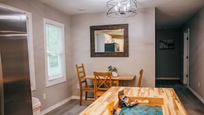 A dining area with a wooden table, chairs, a mirror, and a refrigerator.