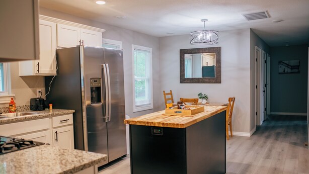 A modern kitchen with white cabinets, a stainless steel refrigerator, a wooden island, and a built-in oven.