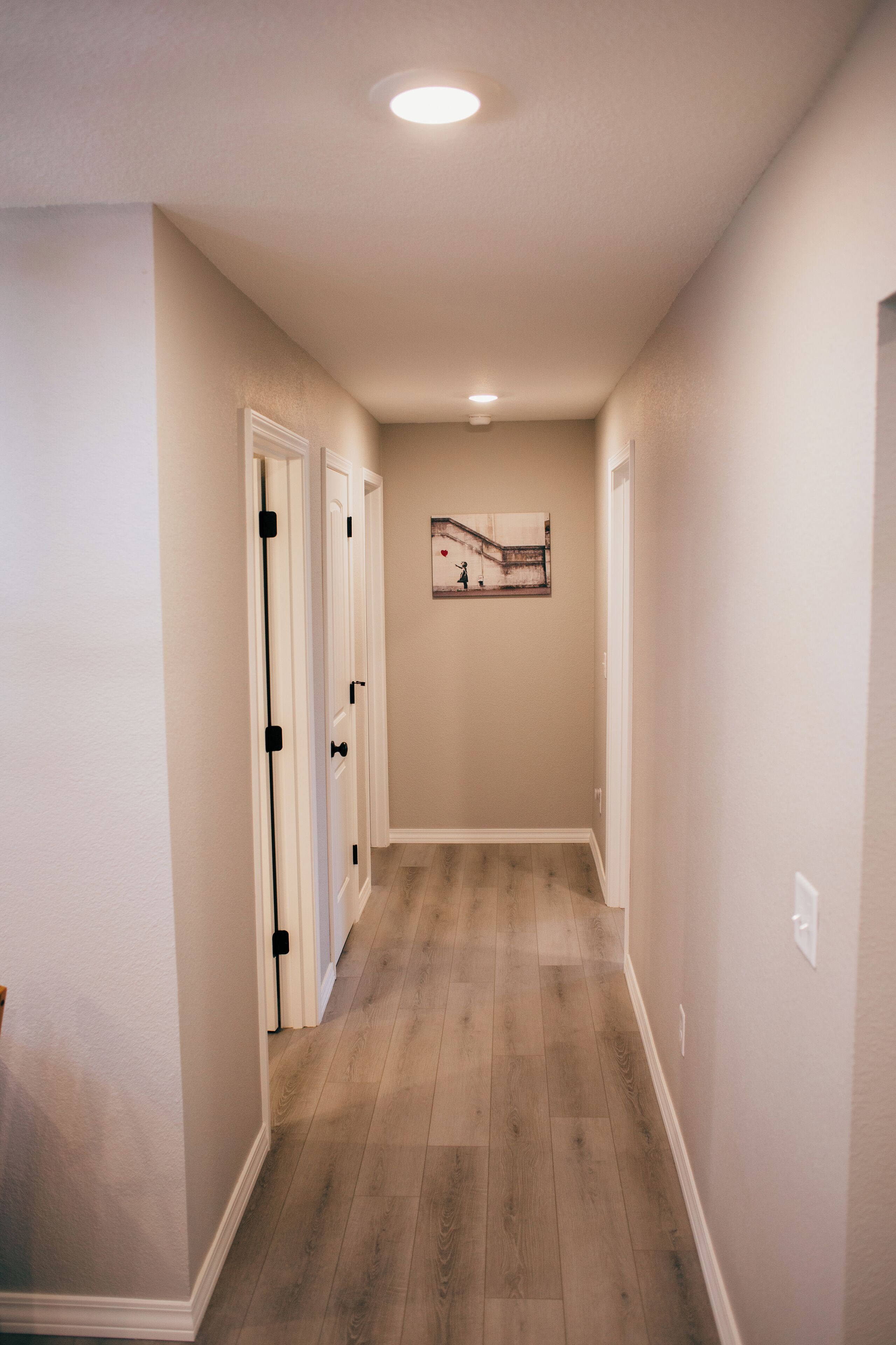 A hallway with wooden flooring, white walls, and a ceiling light.