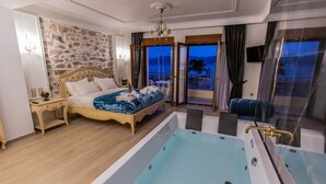 Habitación de hotel con una cama grande, una bañera y vistas a la ciudad al atardecer.
