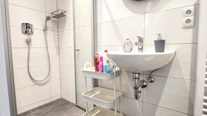 Een moderne badkamer met een inloopdouche, een witte wastafel met spiegel en een klein plankje met toiletartikelen.