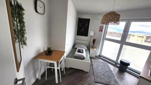Een knus kamertje met een bed, een klein bureau, een stoel, een raam met uitzicht en een hanglamp.