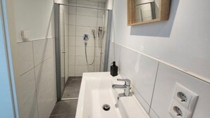 Een moderne badkamer met een douchecabine van glas, een witte wastafel met een spiegel, en een spiegel met houten lijst erboven.