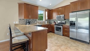 A modern kitchen with wooden cabinets, granite countertops, stainless steel appliances, and a bar area with stools. - Trails End Hideaway Waterfront (Sunrise Beach)
