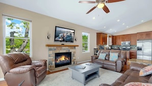 A modern living room with a fireplace, leather sofas, a coffee table, and a kitchen area with stainless steel appliances. - Trails End Hideaway Waterfront (Sunrise Beach)