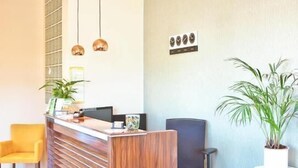 Een receptiebalie van hout, twee hanglampen, een gele stoel, een zwarte bureaustoel en een potplant.