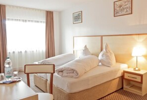 A hotel room with two beds, a desk, a chair, a bedside table with a lamp, and a window with curtains. - Hotel Ganita (Weil am Rhein)