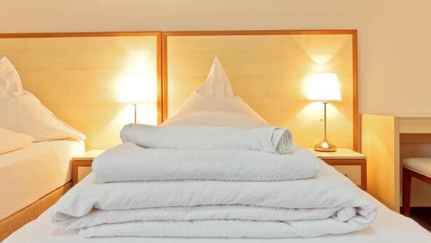 Een hotelkamer met een net opgemaakt bed, twee bedlampen en een stapel witte handdoeken.