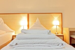 A hotel room with a neatly made bed, two bedside lamps, and a stack of white towels. - Hotel Ganita (Weil am Rhein)