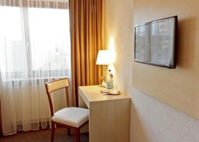 Una habitación de hotel con una silla, una mesita con una lámpara, una botella y un cuadro en la pared.