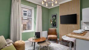 A compact living space with a dining area, a seating area with a sofa and ottoman, a wooden chair, a small round table, and a kitchenette with a microwave and toaster. - Ochill View Apartment by Stirling Train Station (Stirling)