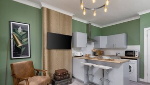 A compact kitchen with a wooden accent wall, a bar area, and a washing machine. - Ochill View Apartment by Stirling Train Station (Stirling)
