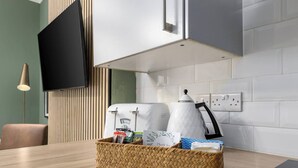 A kitchen with a wooden table, a woven basket with food items, a kettle, and a flat-screen TV mounted on the wall. - Ochill View Apartment by Stirling Train Station (Stirling)