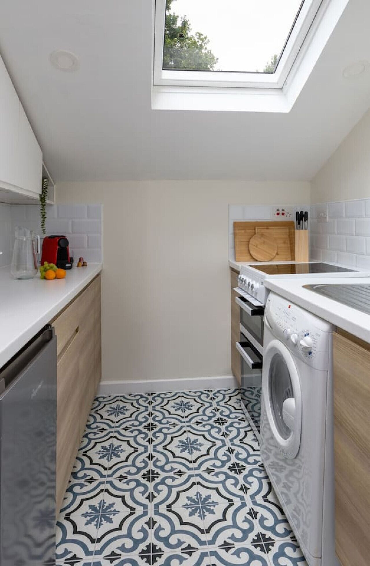 A compact kitchen with a skylight, a washing machine, and a countertop with kitchen utensils.