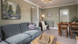 A living room with a grey sofa, a wooden dining table, and a chandelier. - Central Cathedral Apartment (Dunblane)
