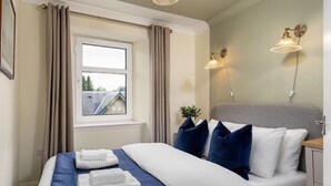 A neatly made bed with blue and white bedding, a grey headboard, and two wall-mounted lamps. - Central Cathedral Apartment (Dunblane)
