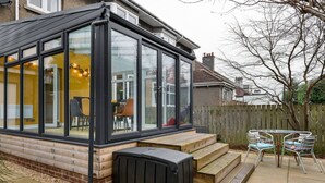 A conservatory with a glass enclosure, a wooden bench, and a table with chairs.