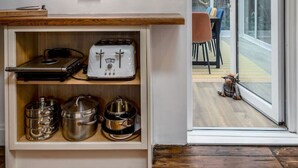 A kitchen with wooden shelves holding kitchenware and appliances, a dining area with a table and chairs, and a glass door leading outside.