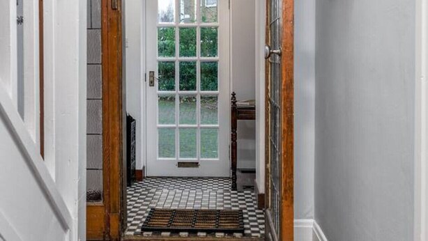 A hallway with a wooden floor, a tiled entrance, and a door leading to a garden.