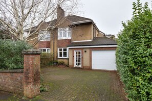 A two-story house with a garage, a brick wall, and a paved driveway.