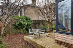 A patio with a table and chairs, surrounded by trees and a stone wall.
