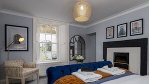 Une chambre à coucher avec un grand lit, un canapé bleu, un fauteuil, une cheminée et des tableaux encadrés accrochés au mur.