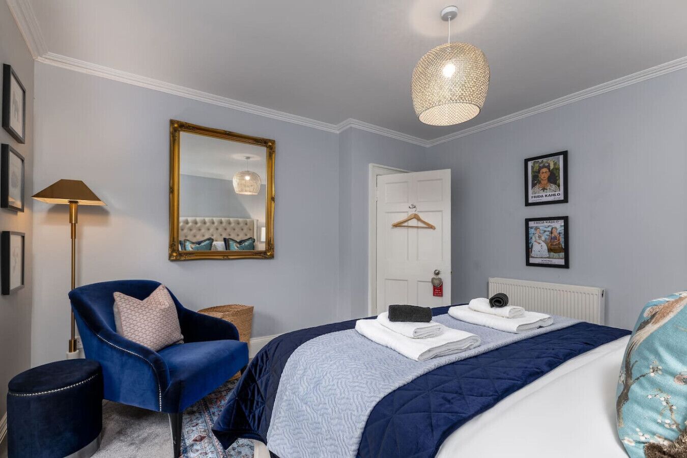 Une chambre à coucher comprenant un lit, une chaise, un miroir, un luminaire suspendu et des tableaux encadrés accrochés au mur.