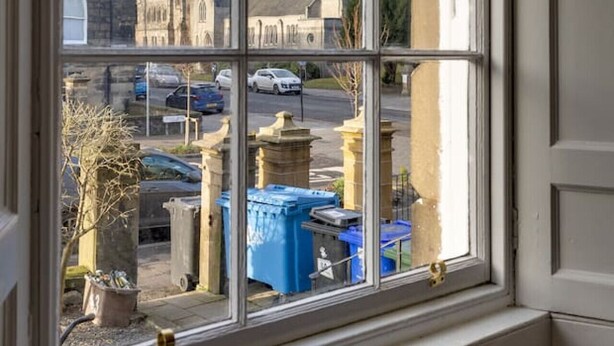 Une fenêtre donnant sur un bâtiment historique et sur des voitures garées à l’extérieur.