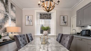 Une salle à manger avec une table en marbre, des chaises recouvertes d’un tissu gris, un lustre et une fenêtre offrant une vue agréable.